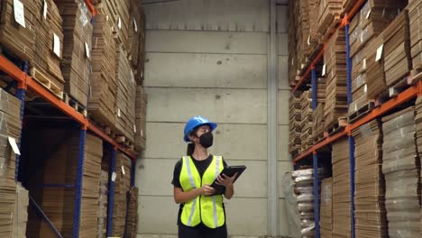 A-female-worker-walking-inside-a-storage-area-of-a-warehouse,-inspecting-the-shelves-while-carrying-a-notepad