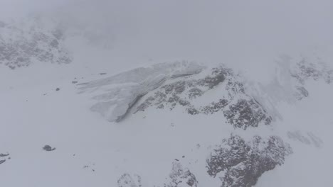 Aerial-view-around-a-glacier-in-the-mountains-with-dark,-blizzard-sky---orbit,-drone-shot