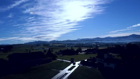 Stimmungsvolle-Sonnenuntergangsstimmung-Mit-Den-Alpen-In-Der-Ferne,-Blick-Auf-Eine-Dunkle,-Sonnenreflektierende-Landschaft-Von-Oben-Mit-Einer-Drohnen-Vogelansicht