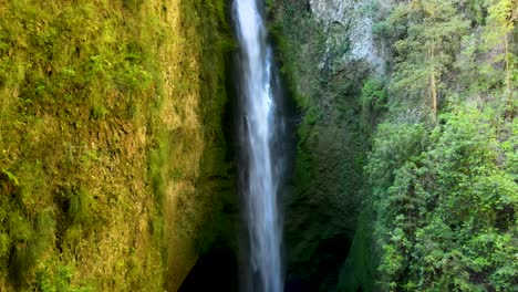 Dolly-out-of-hidden-Mili-Mili-misty-waterfall-falling-into-natural-pool-surrounded-by-dense-green-vegetation,-Coñaripe,-Chile