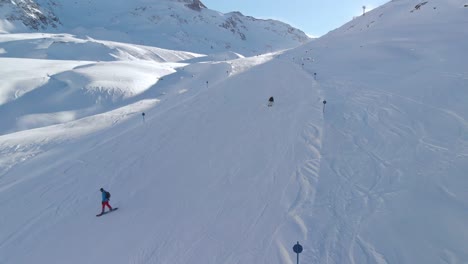 Vista-Aérea-De-Drones-Siguiendo-A-Esquiadores-Y-Snowboarders,-Bajando-Por-Las-Laderas-De-Los-Alpes-Kaunertal,-En-Austria