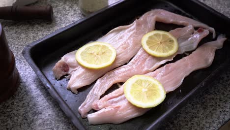 Hands-Placing-Slices-Of-Fresh-Lemon-On-Uncooked-Hake-Fish-Fillet-In-A-Baking-Pan
