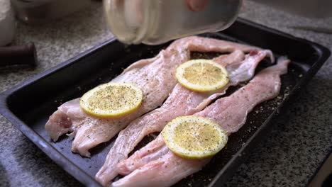 Sprinkling-Spices-On-Fresh-Hake-Fish-Fillet-With-Lemon-Slices-In-A-Baking-Pan