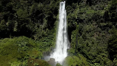 Aerial-dolly-in-of-Salto-El-Leon-waterfall-falling-into-a-natural-pool-surrounded-by-green-dense-forest,-near-Pucon,-Chile