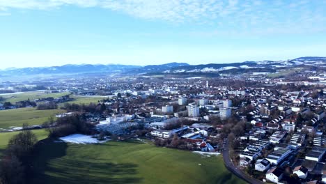Peaceful-city-in-southern-Germany-with-chaotically-laid-out-houses-in-the-foreground,-snow-covered-hills-revealed-after-the-drone-pans-to-the-side
