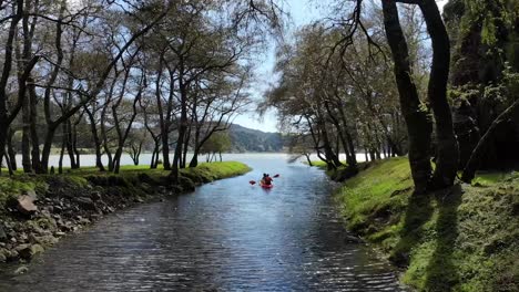Aerial-follow-couple-kayaking-river-stream-surrounded-by-lush-forest,-Furnas-lagoon
