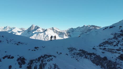 Aerial-view-following-two-ski-hikers,-reaching-the-top-of-mountains,-sunny,-winter-day-in-Austria---rising,-drone-shot