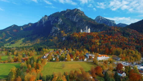 Relaxing-view-of-drone-gliding-up-towards-castle-on-hill-over-scenic-autumn-field-in-the-afternoon-near-the-Neuschwanstein-Castle-in-Germany,-Europe,-wide-view
