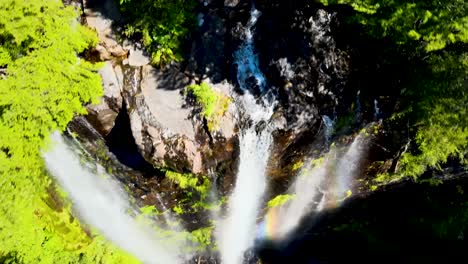 Aerial-dolly-out-of-three-waterfalls-falling-into-rocky-natural-pool-forming-a-rainbow-surrounded-by-dense-green-forest