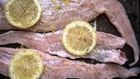 Fresh-Hake-Fillet-In-A-Baking-Pan-With-Lemon-Slices,-Seasoned-With-Ground-Black-Pepper-And-Herbs