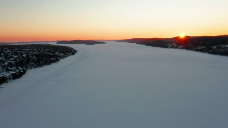 Scenic-aerial-view-flying-over-a-frozen-river-at-sunset