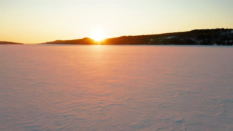 Scenic-aerial-flying-across-a-frozen-lake-as-the-sun-sets-in-the-distance