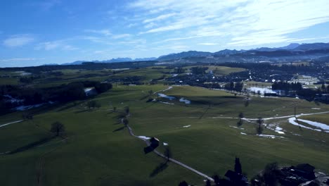 Alpen-In-Der-Ferne,-Blick-Auf-Eine-Grüne-Landschaft-Von-Oben-Mit-Einer-Drohne,-Vogelperspektive