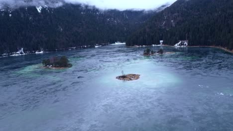 Luftaufnahme-Eines-Atemberaubenden-Zugefrorenen-Sees-Unter-Den-Alpen-Mit-Den-Inseln-Und-Bergen-Im-Schnee