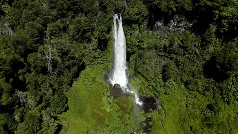 Aerial-dolly-out-of-Salto-El-Leon-waterfall-streaming-on-natural-pool-surrounded-by-green-dense-forest,-near-Pucon,-Chile