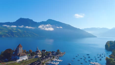 Satisfying-drone-flyover-of-boats-in-pier-on-picturesque-lake-near-medieval-Church-in-Spiez,-Switerzland-in-the-summer,-noon,-wide-view,-europe