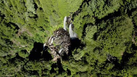 Aerial-top-down-over-three-waterfalls-streaming-into-rocky-natural-pool-surrounded-by-dense-green-woodland