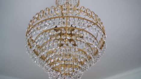 Tilt-down-luxurious-Golden-chandelier-with-crystal-gemstone,-Hanging-on-white-ceiling,-Slow-motion