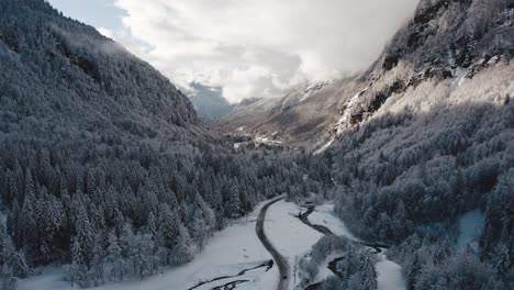 An-Aerial-View-of-Cirque-du-Fer-à-Cheval-while-covered-in-snow-during-a-cold-winter,-tilting-down-and-flying-backwards-to-reveal-the-valley-bed-frosted-forest-and-the-road-that-leads-to-the-circus