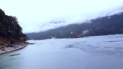Drohne-Fliegt-Tief-über-Einem-Atemberaubenden-Zugefrorenen-See-Unter-Den-Alpen-Mit-Den-Inseln-Im-Schnee