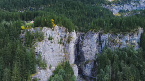 Aerial-drone-view-lowering-above-large-Gletscherschlucht-cave-canyon-system-entrance-in-Grindewald,-Switzerland-at-noon-in-summer,-wide-view