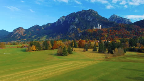 Drone-view-slowly-lifting-up-over-scenic-autumn-field-with-a-distant-castle-on-hill-in-the-afternoon-near-the-Neuschwanstein-Castle-in-Germany,-Europe,-wide-view