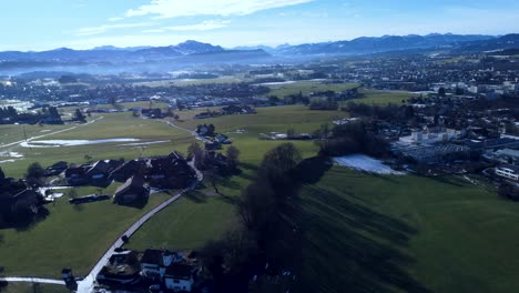 Alps-in-the-distance,-looking-onto-a-green-landscape-from-the-top-with-a-drone,-bird-view