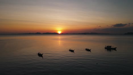 Wunderschöner-Sonnenuntergang-über-Den-Dunklen-Silhouetten-Einer-Insel,-Während-Traditionelle-Thailändische-Boote-Leise-Im-Vordergrund-Schweben