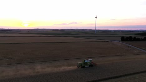Aerial-orbiting-shot-around-industrial-Combine-Harvester-during-work-at-sunset-on-countryside-field---Dust-rising-up-to-sky