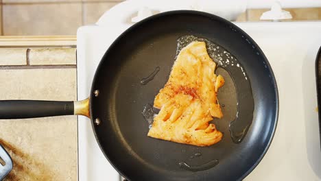 Placing-a-seasoned-salmon-fillet-in-a-frying-pan-with-hot-oil-for-a-tasty-meal---overhead-view