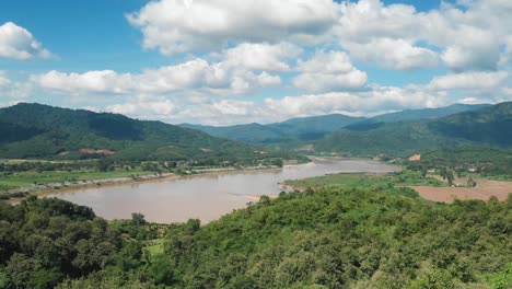 The-Mighty-Mekong-surrounded-by-Mountains-on-a-Blue-Sky-Sunny-Day-Border-of-Thailand-and-Laos,-Drone-Shot
