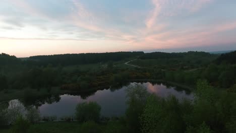 Still-lake-in-a-country-park-at-dusk-on-a-sunset-evening-establishing-revealing-aerial-shot-with-slight-parallax
