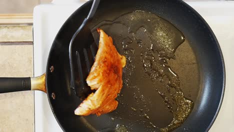Flipping-a-salmon-fillet-in-a-frying-pan-on-the-stove-as-it-sizzles-in-hot-vegetable-oil---overhead-view