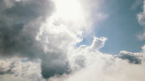 Dünne-Weiße-Wolken-Bewegen-Sich-Sanft-Mit-Dem-Wind,-Während-Im-Hintergrund-Große-Dicke-Graue-Wolken-Langsam-Vor-Der-Sonne-Und-Dem-Blauen-Himmel-Gleiten