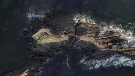 Luftaufnahmen-über-Einer-Felsigen-Insel,-Auf-Die-Wellen-Schlagen