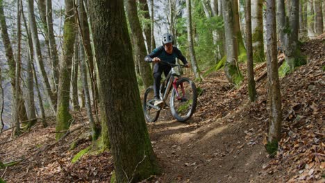 A-mountain-biker-performs-a-tight-turn-through-narrow-trees-in-a-leafy-forest