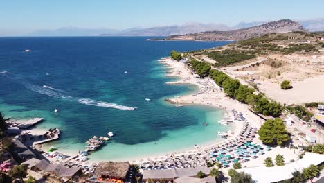 Aerial-Drone-View-of-Ksamil-Beach,-Ionian-Sea,-Albania---Sunbeds,-Jetski,-Hotels-and-clear-blue-sea