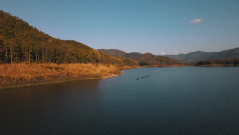 Traditionelles-Thailändisches-Boot-Segelt-über-Das-Blaue-Wasser-Vor-Dem-Hintergrund-Des-Von-Sonnenuntergängen-Beleuchteten-Waldes-Bei-Mae-Ngat-Somboon-Chon-Im-Srilanna-nationalpark