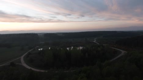 Small-lake-surrounded-by-trees-at-dusk-sunset-Parallax-aerial-shot