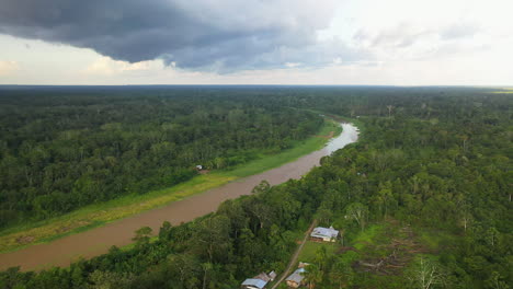 Wide-drone-shot-of-the-Amazon-River-and-rainforest-with-a-few-small-buildings-in-the-forest