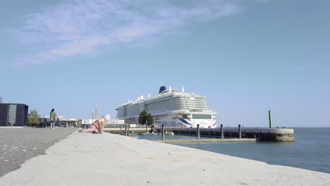 Little-girl-sitting-ground,-huge-cruise-ship-in-background,-Lisbon,-Portugal