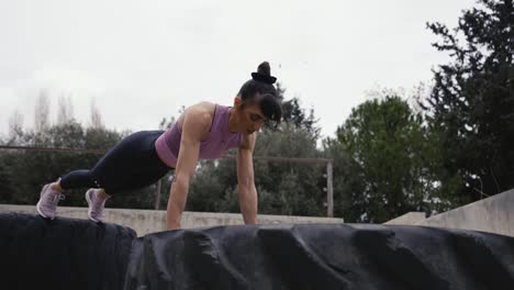 Athletic-young-woman-performing-push-ups-on-Tyre-exercising-outdoor-at-sportsground-enjoying-physical-activity