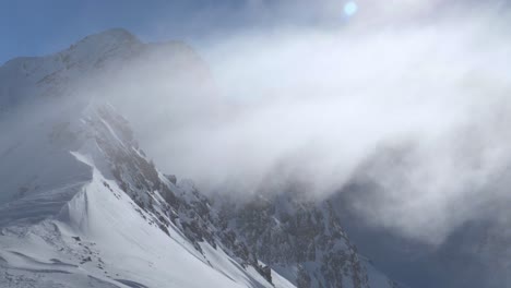 fog-cloud-moving-over-a-rocky-mountain-ridge,-sunny-day,-high-in-the-alps---pan-view