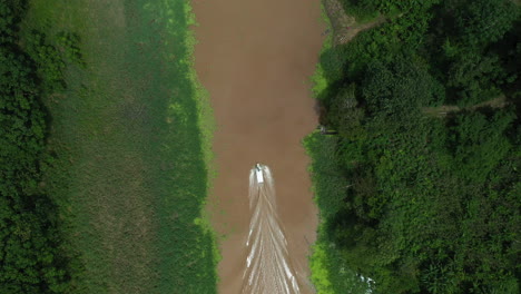 Cinematic-downward-angle-drone-shot-with-a-boat-with-wake-on-the-Amazon-river-and-the-rainforest-surrounding-the-river-in-Peru,-following-shot