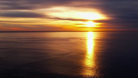 Golden-sunrise-over-the-Eastern-horizon-reflecting-off-the-surface-of-the-tranquil-ocean---descending-aerial-view