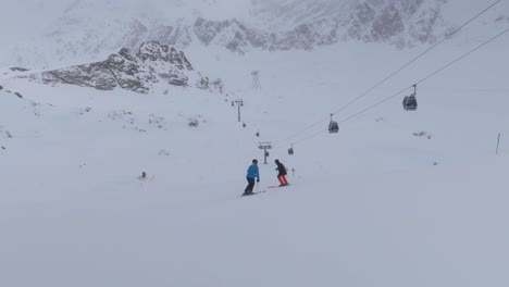Skiers-riding-down-cloudy-mountain-slopes-with-ski-lifts-in-the-alps---pan-view