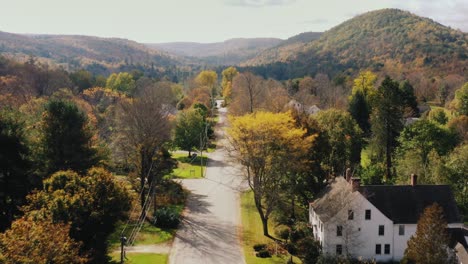 Aerial-drone-shot-over-a-road-with-rows-of-ouses-on-both-sides-in-Litchfield-County,-Connecticut,-United-States-with-the-view-of-hilly-terrain-in-the-background