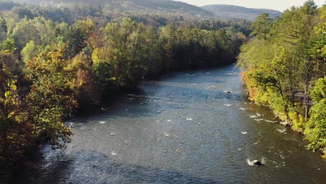 Drone-tilt-up-shot-of-Housatonic-river-passing-by-with-dense-forest-on-both-sides-in-the-hilly-terrain-in-Litchfield,-Connecticut,United-States-on-a-sunny-morning