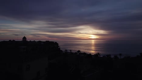 Silhouette-layers-Cabo-resort-city-aerial-view-rising-to-glowing-sunrise-skyline-and-shimmering-Gulf-of-California