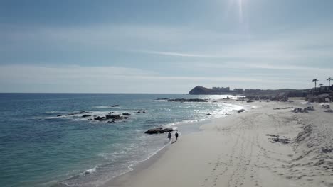 Two-people-walk-on-Cabo-San-Lucas-Beach-in-Mexico,-Baja-California